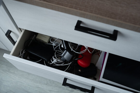 Charging cables and adapters lie tangled inside a white storage box, representing everyday tech clutter and the need for organization. Home organization blogs, cable management product ads