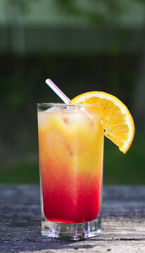 Tequila sunrise cocktail with straw and orange slice outdoors
