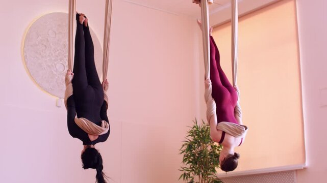 Flexibility training. Hammock yoga. Woman hanging upside down doing synchronous fitness session in studio rotating with fabric equipment support.