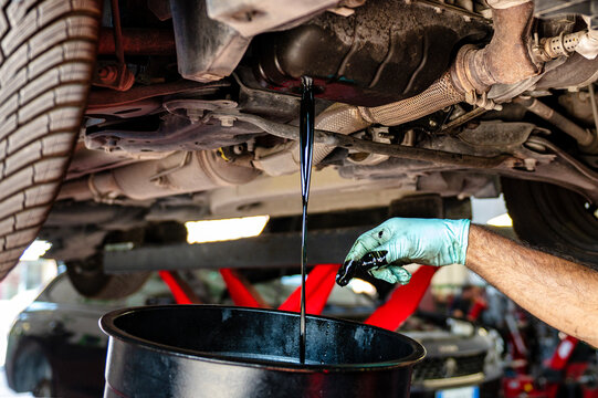 Mechanic performing an engine oil change while used motor oil drains from the oil pan into a collection container in an automotive repair workshop