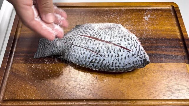 A chef's hand sprinkles rock salt onto fish,