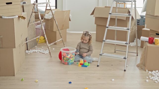 Little girl playing with colorful building blocks from a plastic tub and lifting a red lid in building; playful curiosity.