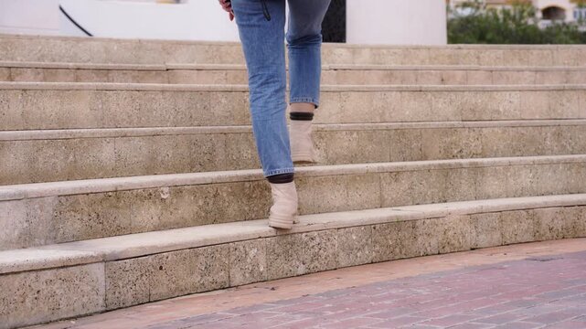 Young woman in jeans, boots, and jacket confidently walking up outdoor city stairs. Concept of personal growth, moving forward, success, determination, urban lifestyle, independence, achieving goals