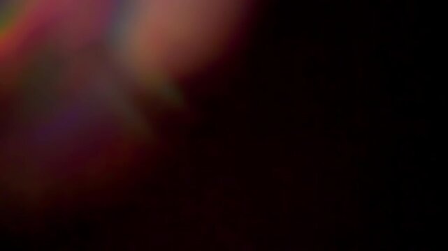 Abstract video of a concentric rainbow prism flare gently pulsing and drifting over a dark background, creating soft ethereal light leak effects for overlays, transitions, and motion graphics.
