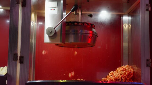 Popcorn machine making fresh buttery popped corn inside a glass case with a red background, a classic cinema snack food preparation process showing the falling kernels