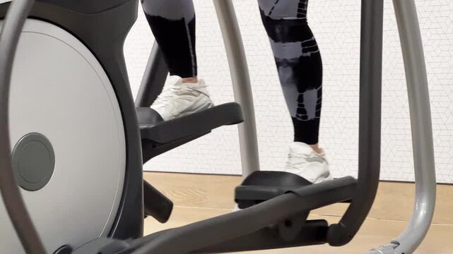 A woman uses an elliptical machine at a gym while focusing on her workout. She shows proper form and engages in fitness activities.