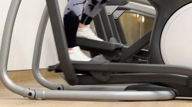A person exercises on an elliptical machine in a gym. The workout helps to enhance fitness levels. The gym is active with morning energy.