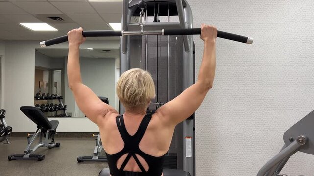 A person performs pull-up exercises on a machine at a gym. The session shows various angles of the workout.