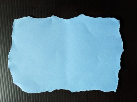 torn paper background. Torn blue paper with jagged edges on dark ridged surface, highlighting texture, contrast and minimal design elements