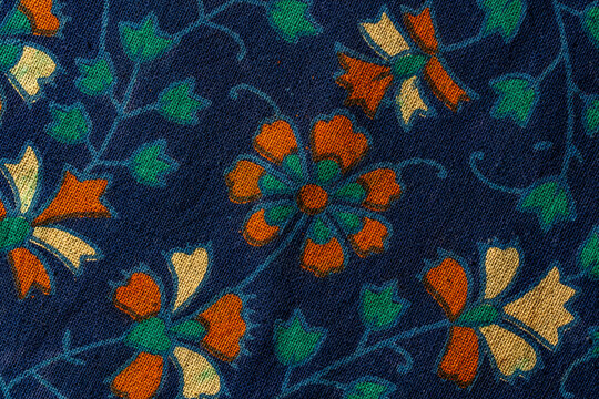 Vintage floral pattern on dark blue fabric texture. Macro of dark blue textile background with floral ornaments in orange beige and green colors representing vintage style or ethnic interior decor