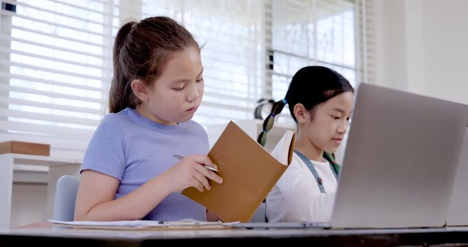 Caucasian preteen girl reading folder while asian girl typing on laptop in classroom illustrating teamwork collaboration education study project digital learning childhood productivity communication