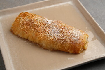 Fototapeta premium Golden sesame pastry roll dusted with powdered sugar on beige