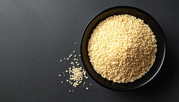 Raw creamy white proso millet grains in a black bowl on a dark background