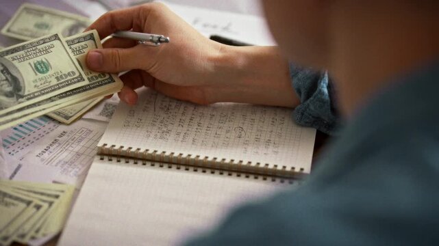 A middle-aged accountant meticulously reviews financial entries in a diary, holding cash dollar bills, ensuring accuracy in finance control and tracking money movement for secure transactions