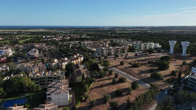 Aerial overview of residential complex resort buildings in Vilamuora, Algarve, Portugal, Europe. Shot of rooftops of luxury cottages in green landscape with mountains on background. Golf fields.