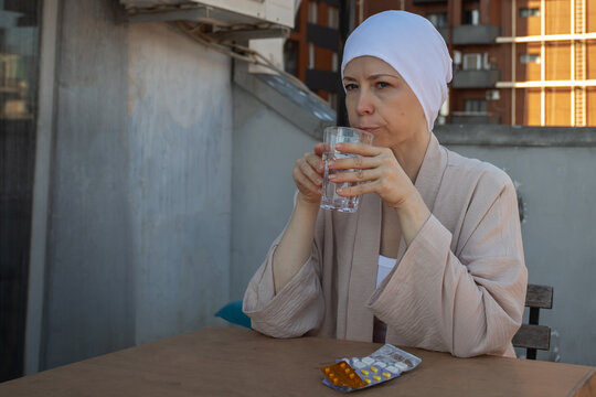 cancer patient drinks water after medicine at a sunlit balcony table, with pills in blister packs, representing prescribed therapy, chronic disease care and resilience