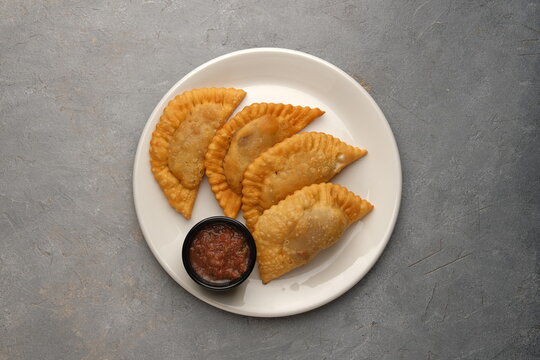 White plate of golden fried turnovers with red dipping sauce