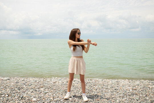 teenage girl stretches on a pebble beach by the sea, showing light coastal exercise, summer fitness, warm up before sport and healthy active travel by the water
