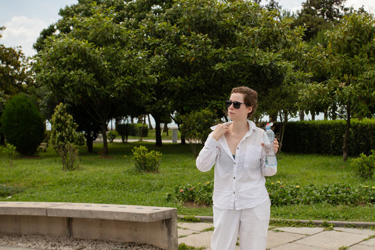 adult cancer survivor pauses with portable water in a public park, symbolizing heat management, energy pacing and daily recovery routines during a warm day of outdoor rehabilitation