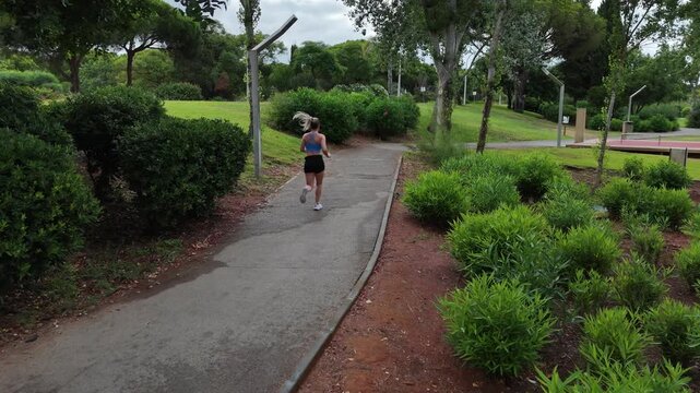Female runner in activewear burning calories with a cardio workout. Sporty woman jogging running on city park bridge outdoors. Woman exercising with earphones on in the morning. Copy space Stock Photo