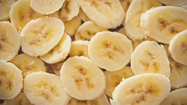 Bright yellow banana slices are casually layered in multiple rows across the frame, their smooth texture highlighted for a food-photography shoot that celebrates fruit freshness and visual detail