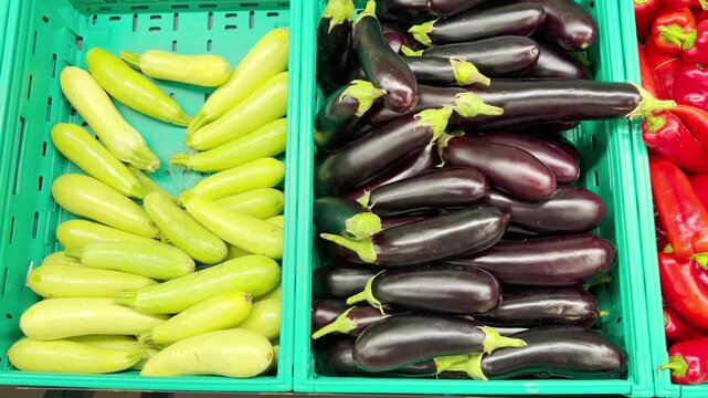 Colorful Display of Fresh Bell Peppers and Purple Eggplants in Plastic Containers on a Supermarket Shelf