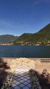 Elegant Lake Como outdoor wedding ceremony with a white aisle leading to a floral arch. Surrounded by guests, mountains, and lake views, capturing a luxury destination wedding moment in Italy.