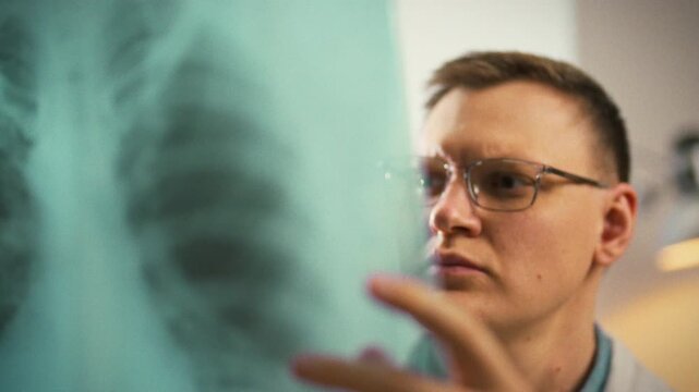 Doctor carefully examines patient's lung x-ray on bright clinic screen, scanning shadows for disease. This focused examination supports diagnosis, underscoring imaging's vital role respiratory care