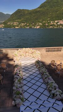 Elegant Lake Como outdoor wedding ceremony with a white aisle leading to a floral arch. Surrounded by guests, mountains, and lake views, capturing a luxury destination wedding moment in Italy.