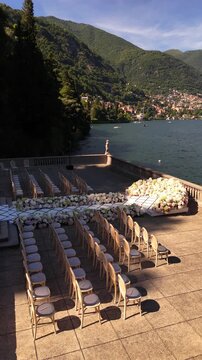 Luxury destination wedding setup on Lake Como with a white aisle leading to a floral arch. Guest seating arranged facing the lake and mountains, creating a cinematic Italian ceremony view.