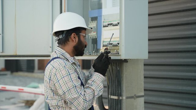 Indian electrician inspecting electrical fuse box outdoors