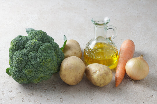 Fresh raw broccoli, potatoes, carrot, onion and olive oil ingredients on light stone background. Healthy vegetables and cooking ingredients for homemade meals and soups