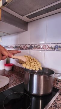 Close up view of a man's hands putting uncooked gnocchi into a stainless steel pot with boiling water, showcasing the process of cooking a traditional Italian potato pasta dish