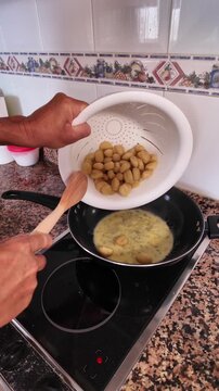 Slow motion footage of a man's hands pouring fresh potato gnocchi from a colander into a hot pan with melted gorgonzola cheese sauce, preparing a classic Italian dish in a home kitchen