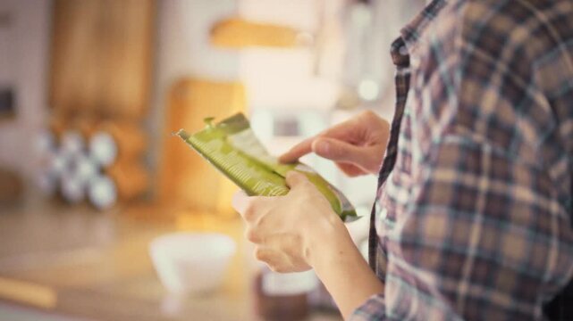 In a bright home kitchen at midday, a girl inspects the soft plastic packaging of a food product, scrutinizing its composition to ensure proper nutrition and make a conscious, healthy food choice