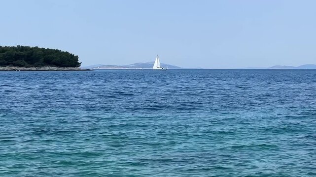 Sailboat moves across water near coastline on a clear day in Croatia