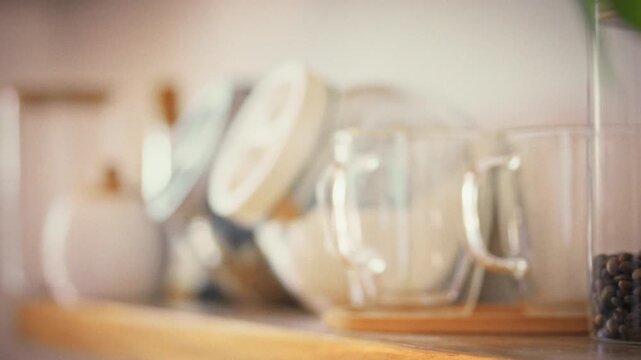 In a neatly arranged kitchen, a woman's hand stretches toward a signed granola jar on the shelf, part of her calm morning ritual that highlights orderly food prep and a mindful approach to nutrition