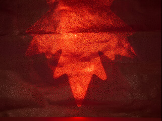 Bright red light creates a star shape on a textured background in a dimly lit space during a festive event © Piotr