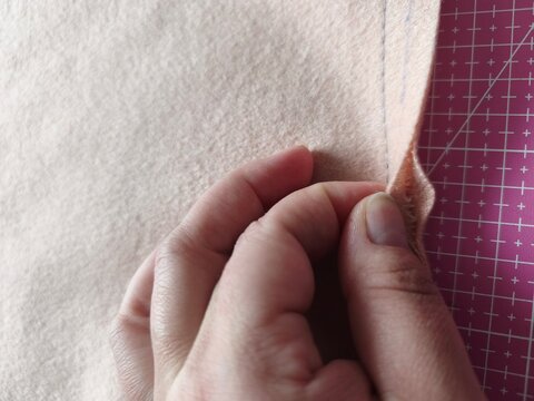 Close-up of a tailor hand stitching the edge of a double-faced wool coat fabric on a pink cutting mat