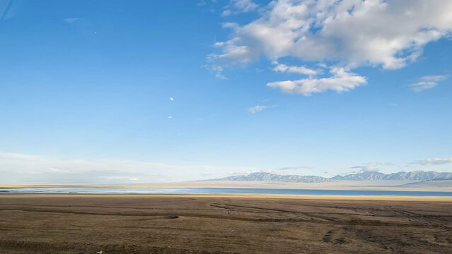 Serene blue high altitude salt lake reflecting a clear sky and distant mountains with a faint moon