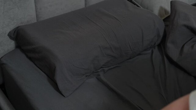 A man in his 30s lies in bed and wakes up, stretching his arms before getting up. The person is happy in the morning and looks well-rested