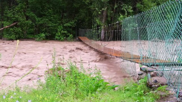 Flash flood and mudflow in Turgen Gorge, Almaty region, Kazakhstan. Raging muddy river current near a suspension bridge. Editorial, travel, and environmental disaster background with copy space.