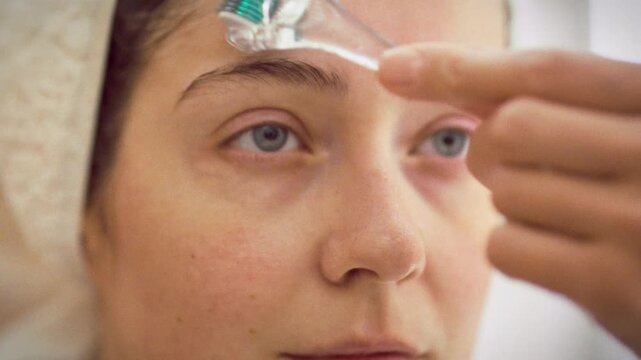 In home spa, young woman rolls a derma roller with microneedles across her face, delivering a facial massage that stimulates skin, enhancing tone and condition as part of modern skincare rejuvenation