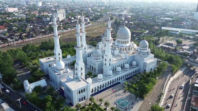 Aerial view of Sheikh Zayed Grand Mosque in Surakarta with urban traffic, cars, motorcycles, and train on railway track at sunset, Solo, Central Java, Indonesia. Cinematic drone infrastructure shot.