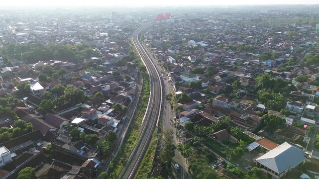 Aerial view of railway tracks cutting through Surakarta city center at sunset, Solo, Central Java, Indonesia. Drone shot of urban railroad infrastructure during warm afternoon light.