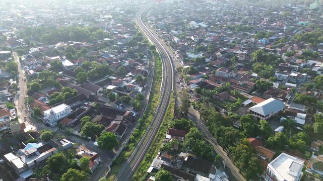 Aerial view of railway tracks cutting through Surakarta city center at sunset, Solo, Central Java, Indonesia. Drone shot of urban railroad infrastructure during warm afternoon light.