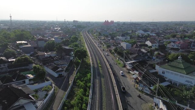 Aerial view of railway tracks cutting through Surakarta city center at sunset, Solo, Central Java, Indonesia. Drone shot of urban railroad infrastructure during warm afternoon light.