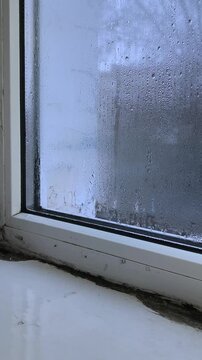 mold on glass, caused by unchecked humidity and water seepage. Streaks and spots of black mold run vertically along a windowpane. old condensation an abstract pattern of neglect. vertically