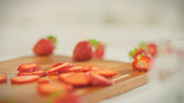Slicing ripe red strawberries into thin slices on a cutting board in a bright kitchen. A man prepares fresh, sweet berries as an ingredient for a dessert, baked goods, or summer smoothie
