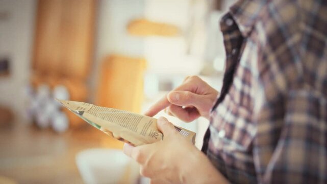 Studying the label on a soft package, a young woman in a bright home kitchen checks the nutrition facts, ensuring the product's composition aligns with her responsible health approach